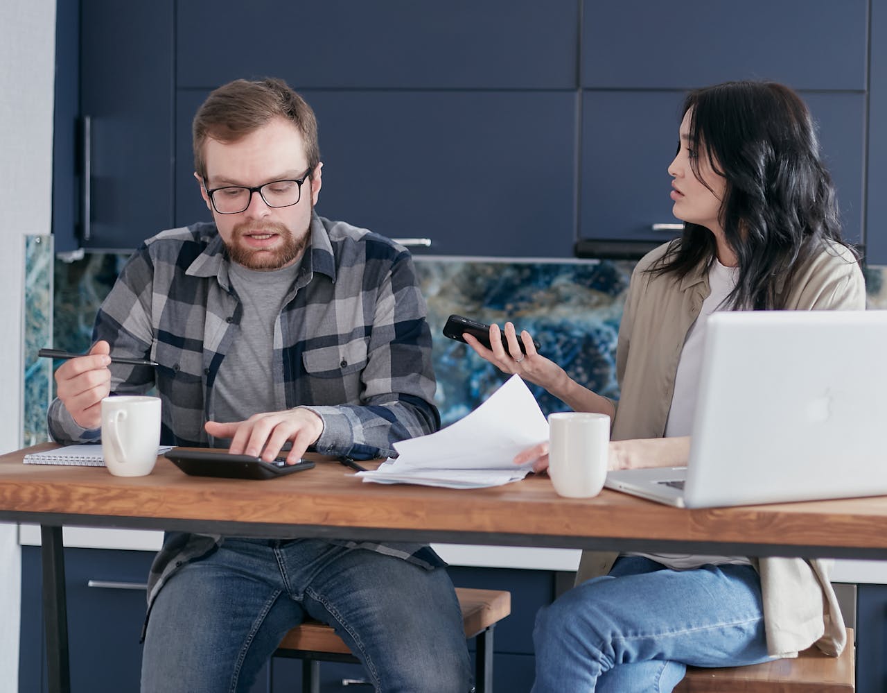 Two colleagues engaged in a work discussion around an office table, using a calculator and documents.